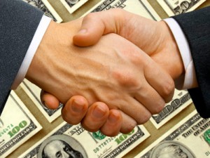Shaking hands in front of pile of money